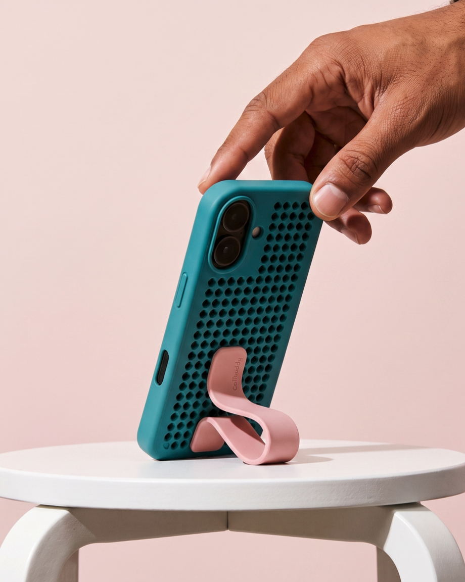 Teal perforated phone case with pink strap standing on a white table