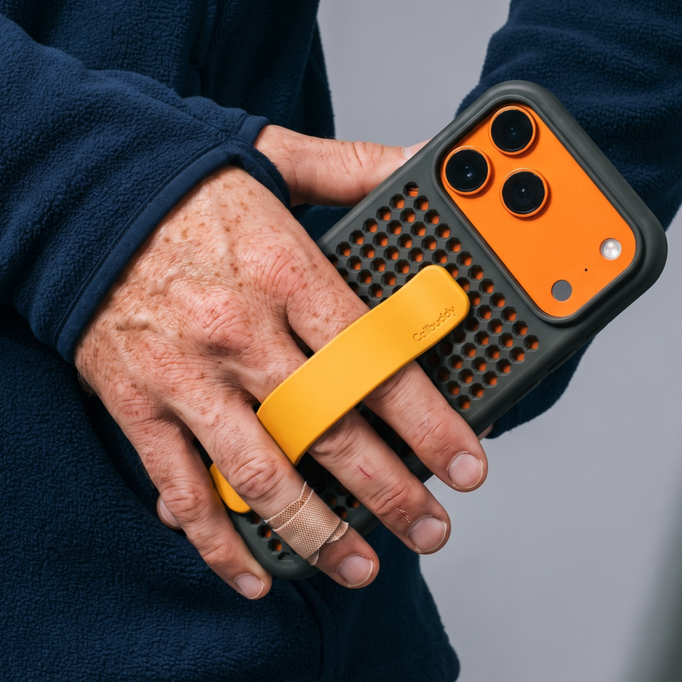Hands holding the grey perforated phone case with orange accents and yellow strap