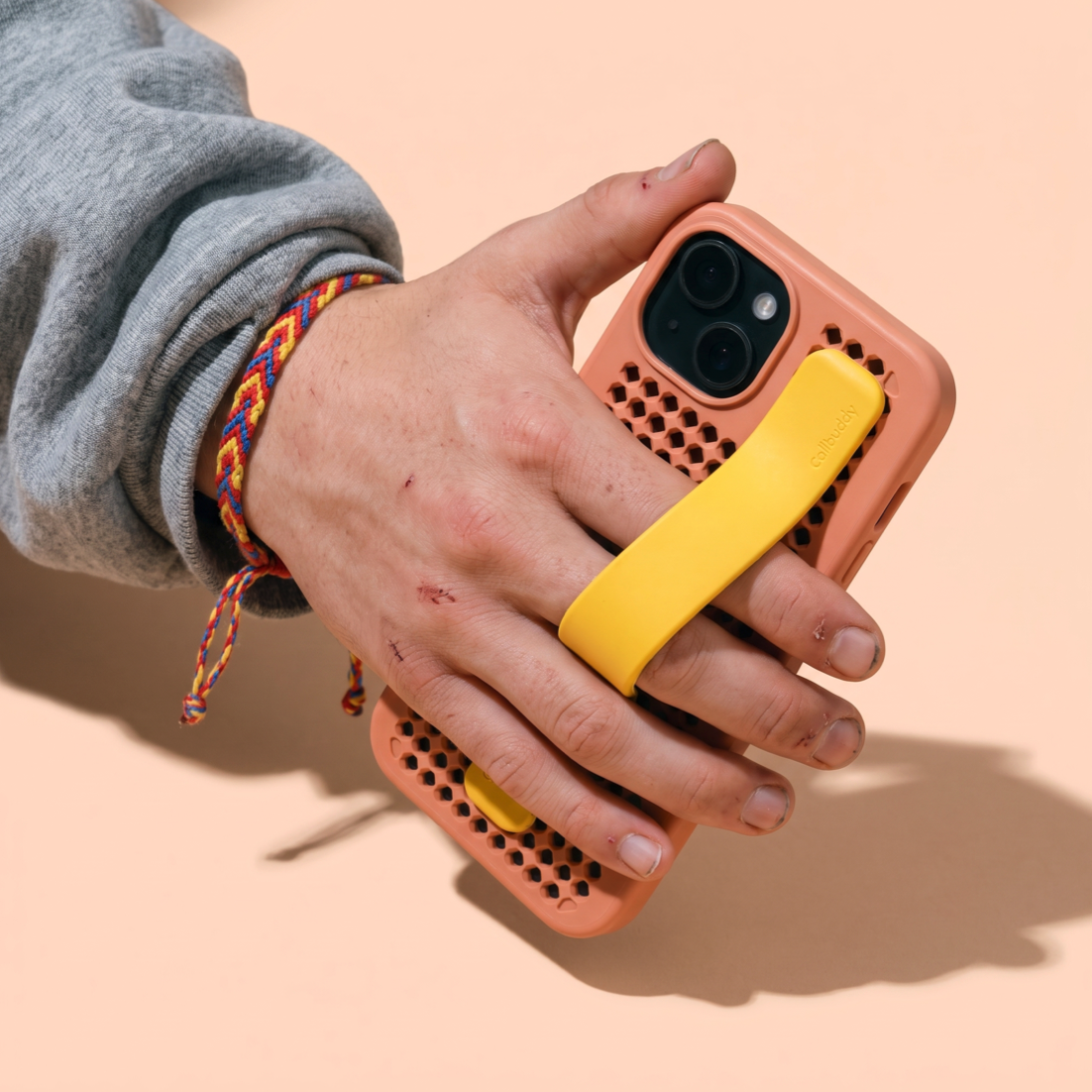 Hand holding the coral perforated phone case with yellow strap