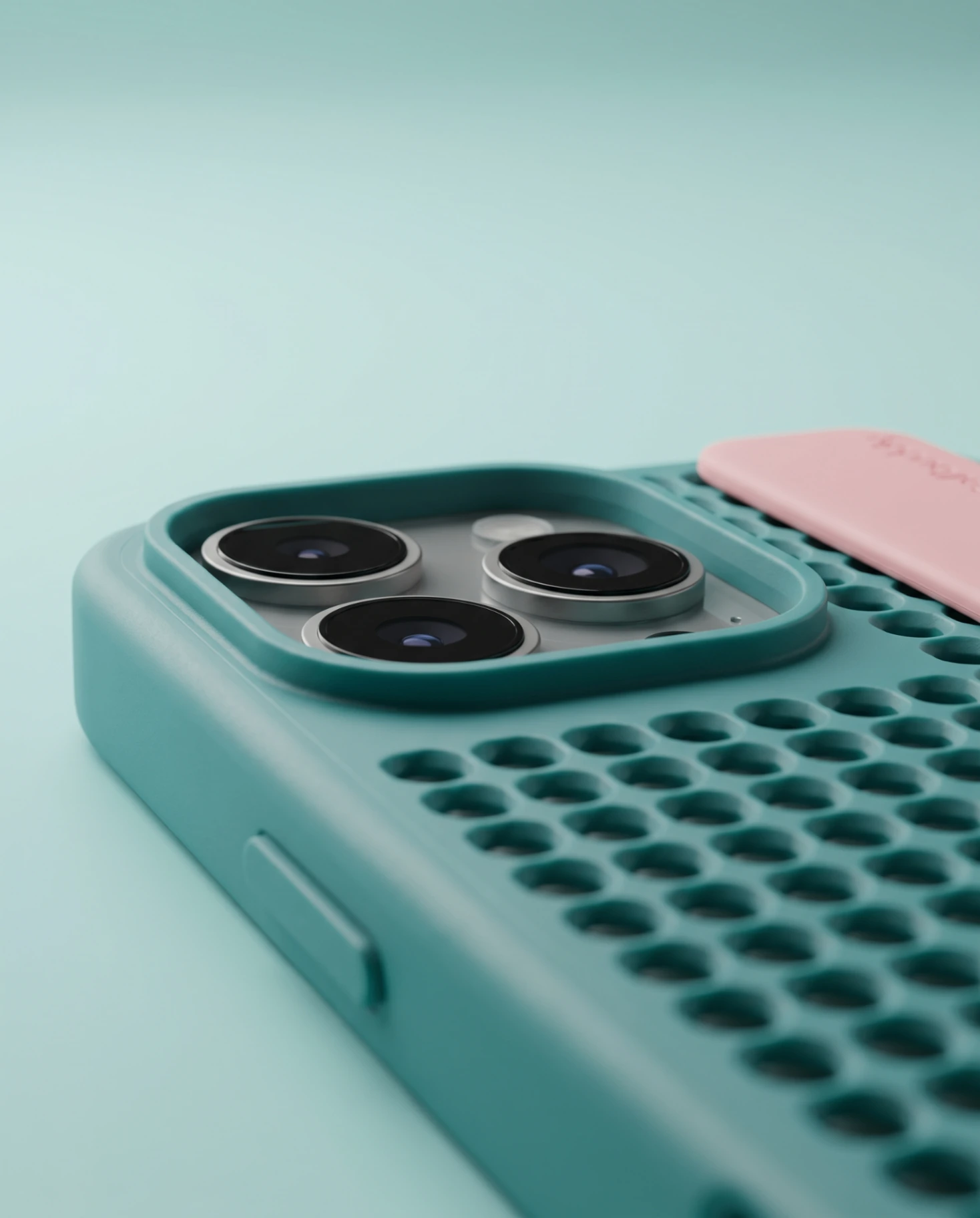 Macro close-up of a teal Callbuddy case with raised camera protection and honeycomb texture, beside a pink strap